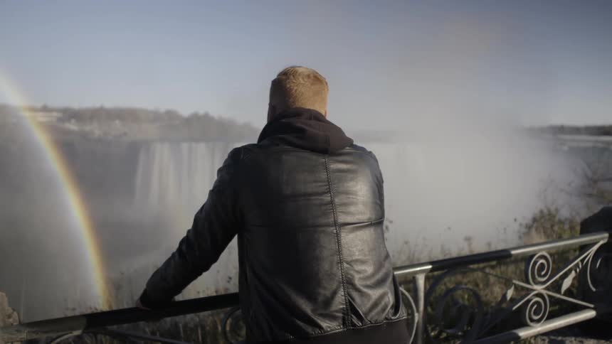 A man leans on a guard rail overlooking a rainbow