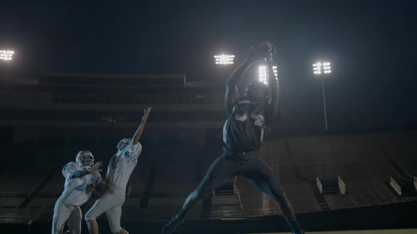 A football receiver jumps up to make a catch under the lights