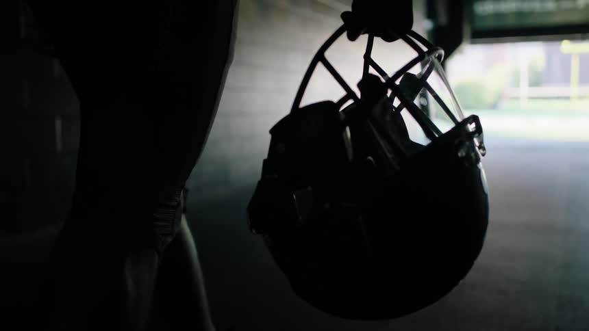Person walking down a hallway holding a football helmet