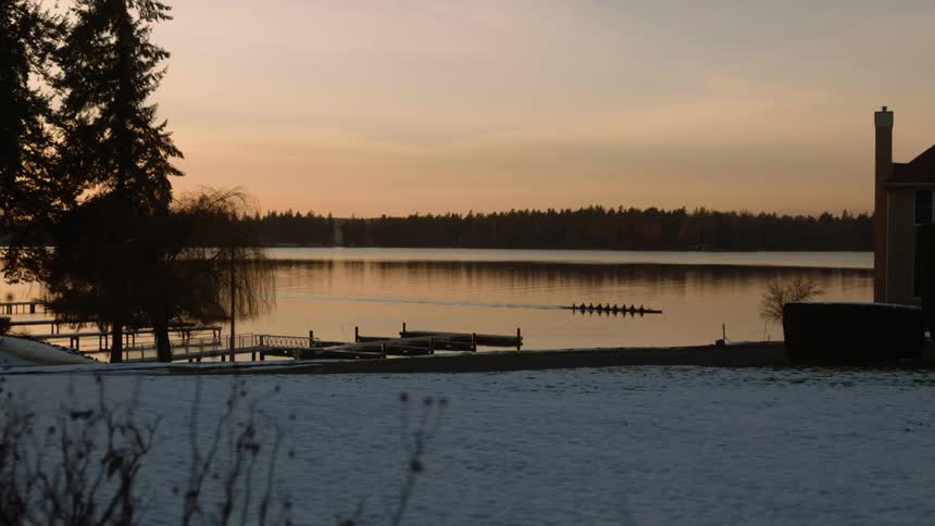 Rowing team paddling boat across lake at dawn in winter