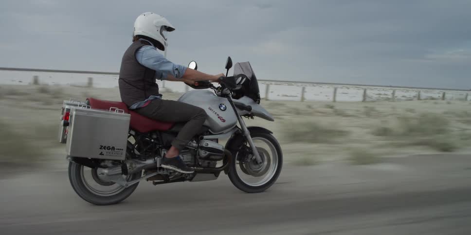 A man is riding a motorcycle down a road on a cloudy day