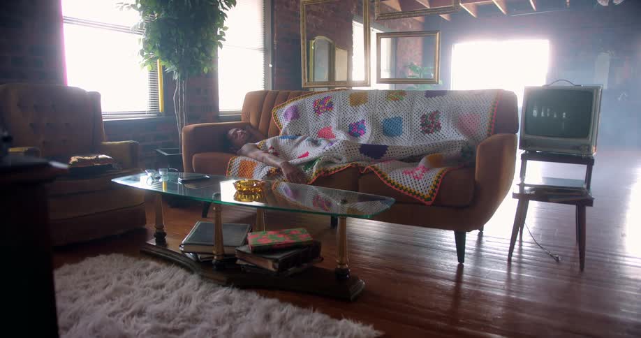A man sleeps on a sofa beneath a group of empty picture frames suspended in midair