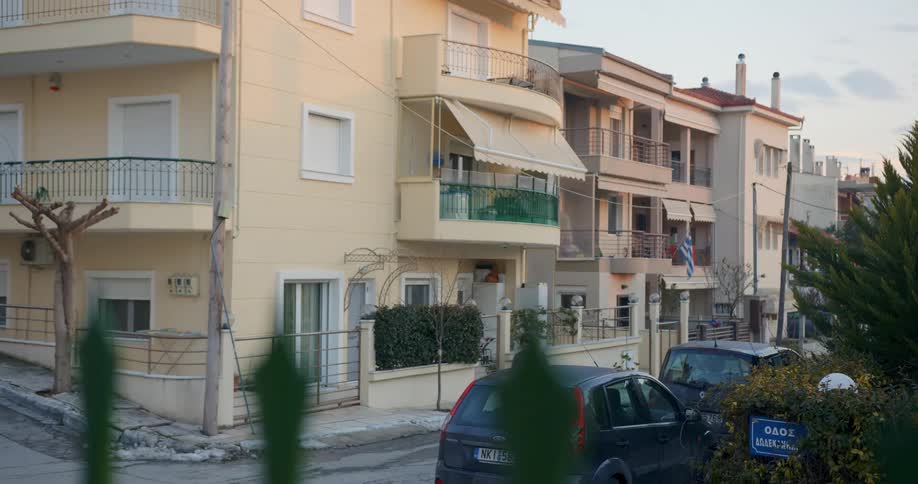 A woman walks on the road next to cars and an apartment building