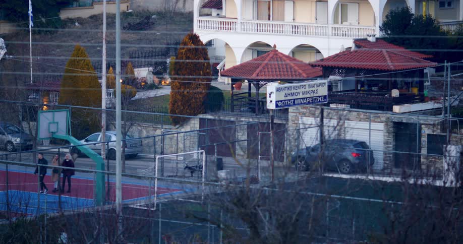 Pedestrians walk across basketball court near store with sign and apartment building