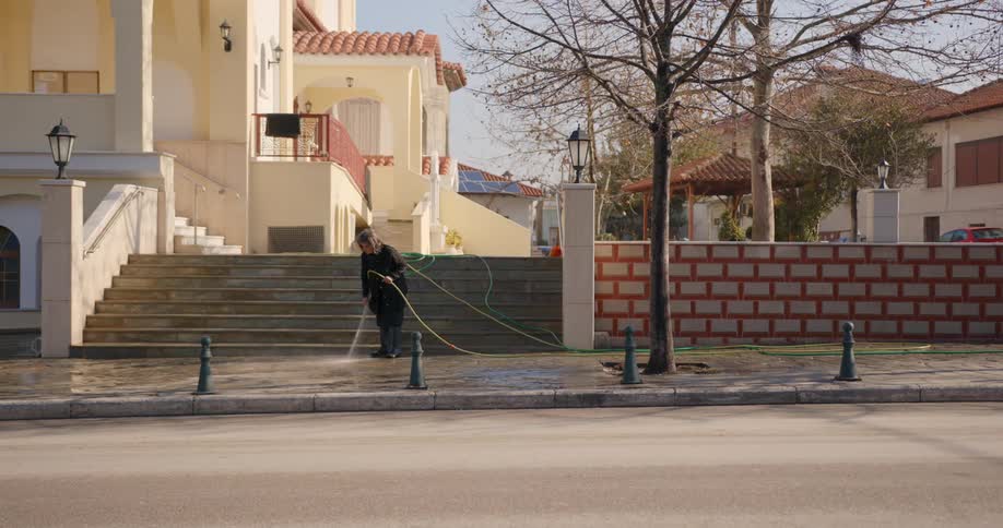 A person uses a garden hose to spray water on a sidewalk