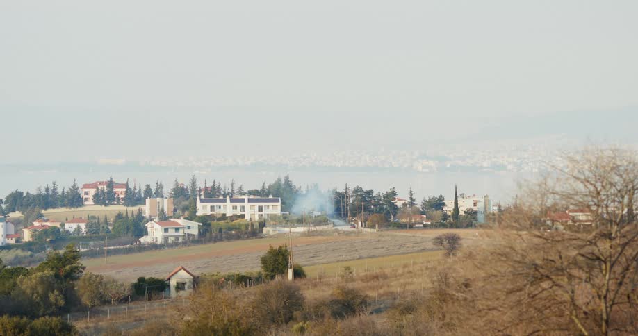 Smoke rises near large building sitting near empty mowed field in town