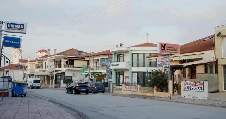 Vehicles pass a road in a small town with a row of business buildings