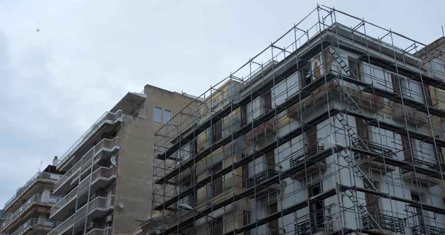 Birds fly over a building with scaffolding covering the exterior