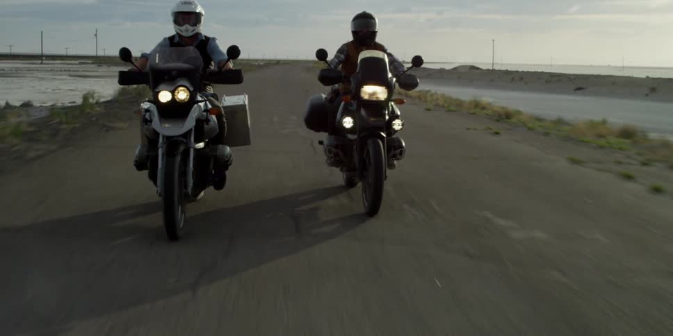 Two people ride down a pavement road on motorcycles