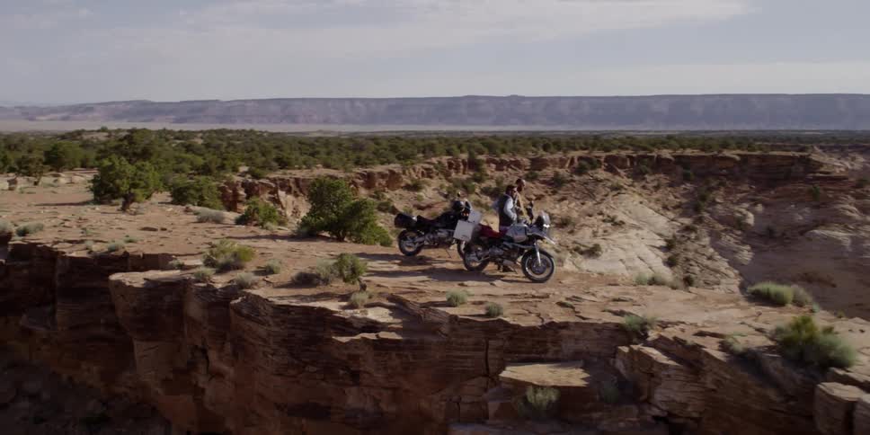 Two people are overlooking the view from a cliff with their motorcycles
