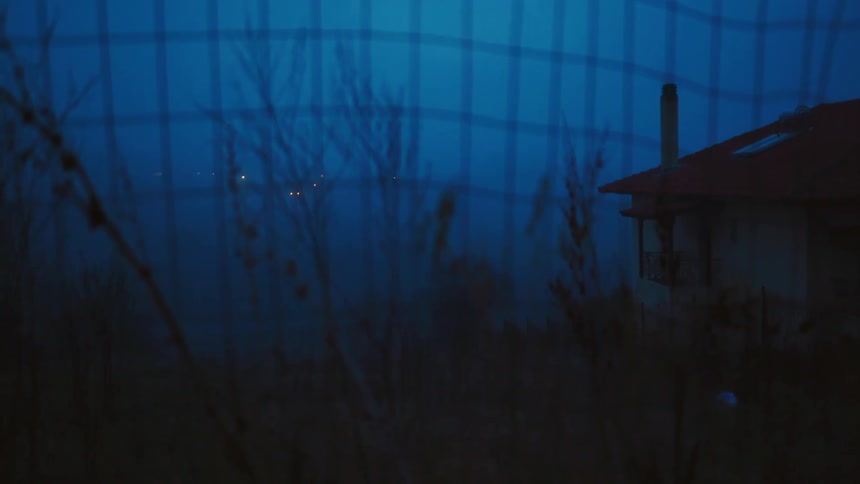 Leafless trees occupy backyard of red roofed house while city lights shine in distance