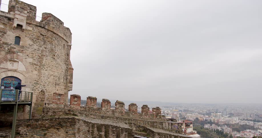 Two people standing by a castle with buildings the sky and clouds in the background