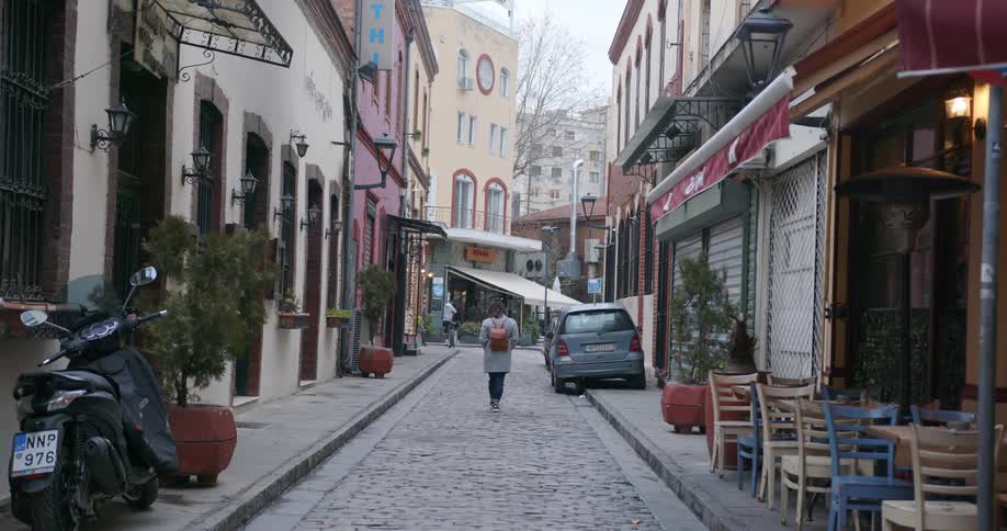 Person walks down brick side street in city neighborhood with cafe