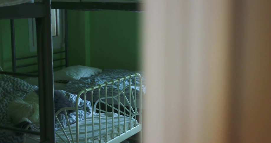 Two metal beds with thin mattress sit side by side under a metal loft bed to create a bunk bed style