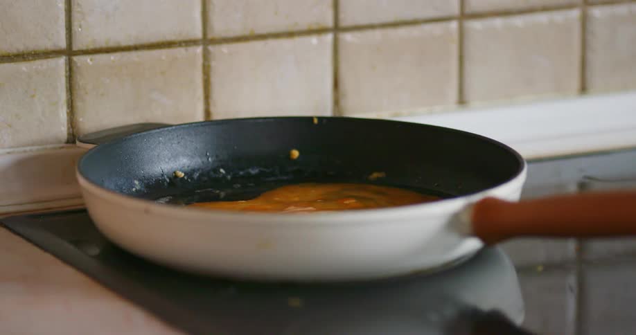 A person pouring eggs into a frying pan on the stove and mixing it with a spatula