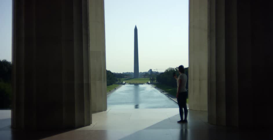 A woman uses her smartphone to film the lincoln memorial pool and washington monument