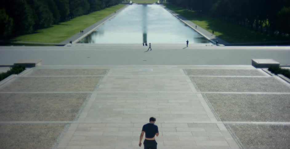 A man wipes his face with his shirt while descending a stone staircase in front of the lincoln memorial reflection pool