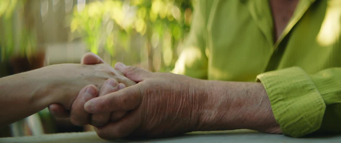 Two people sitting at a table and holding hands with plants in the background