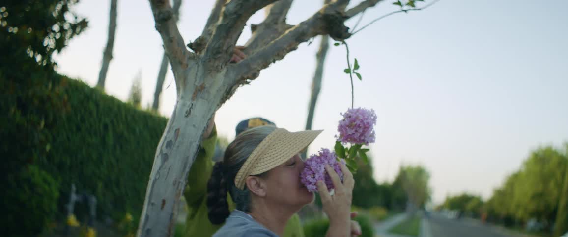 An elderly man pulls a branch down so his wife can smell the flowers