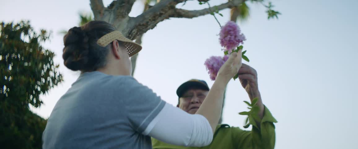 Man and woman smell flower on tree branch smiling