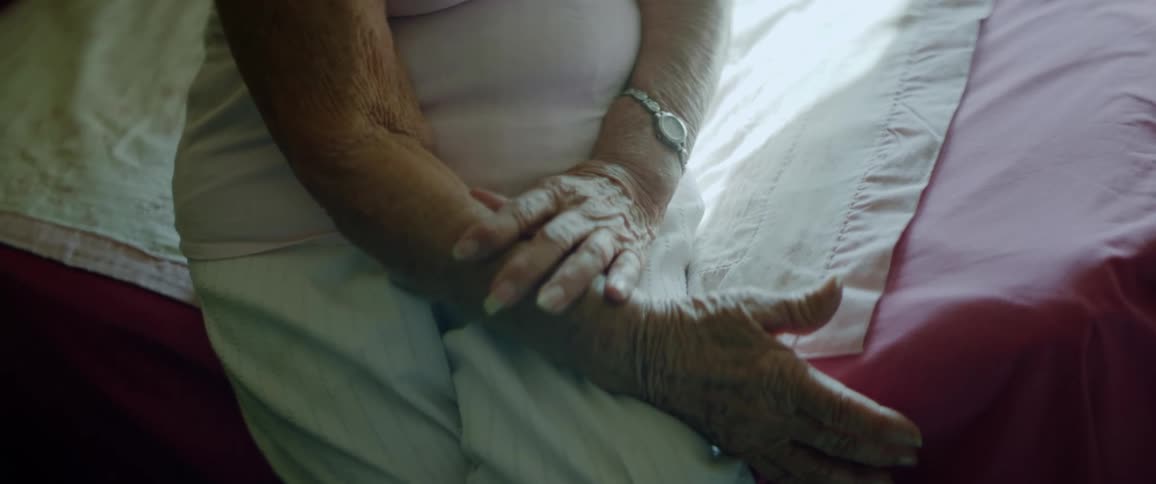 Elderly woman sitting on bed with hands in lap