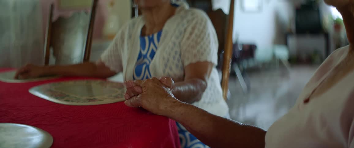 Two elderly women holding hands at table