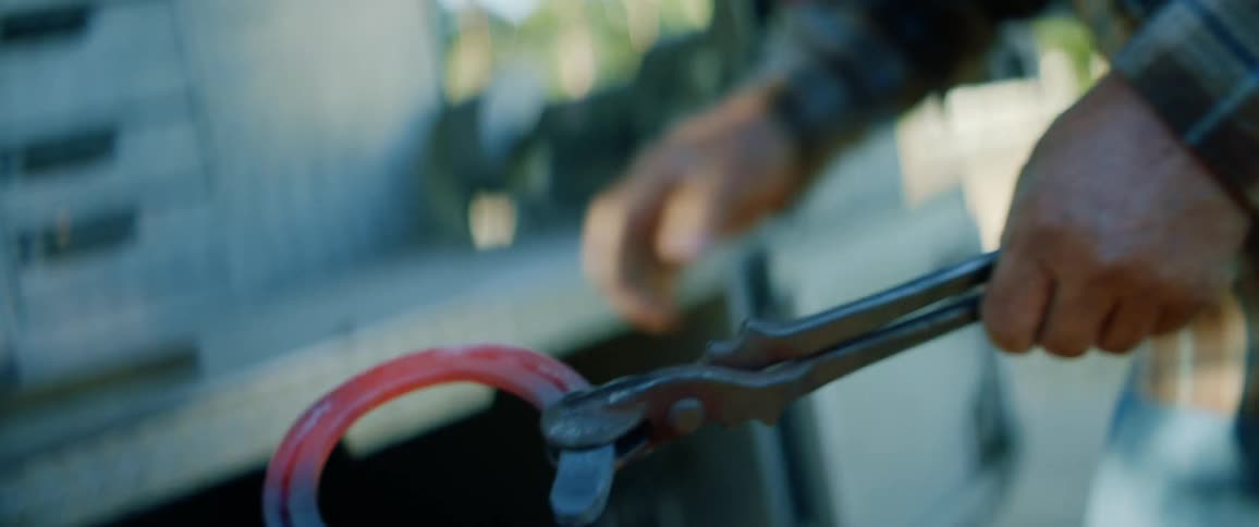 A man pulls a horse shoe out of a fire and hammers on it