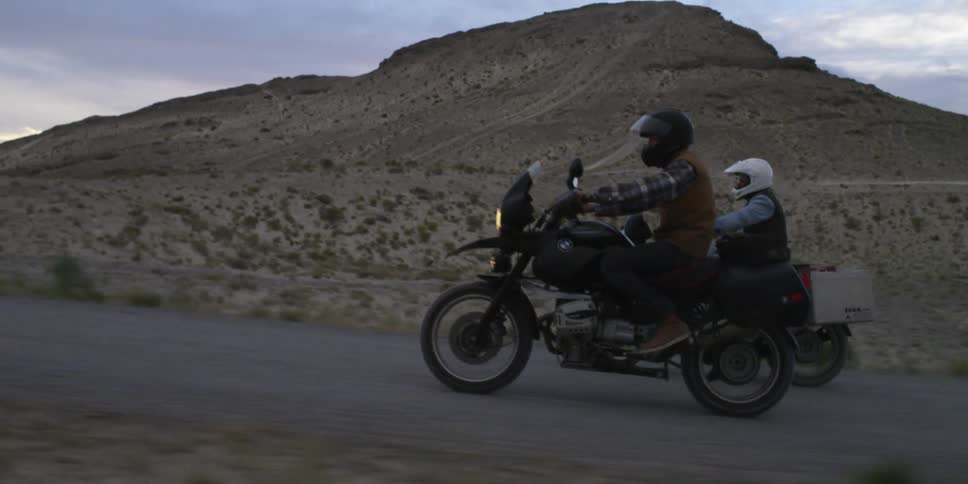 Two motorcycles drive down a small road at sunset