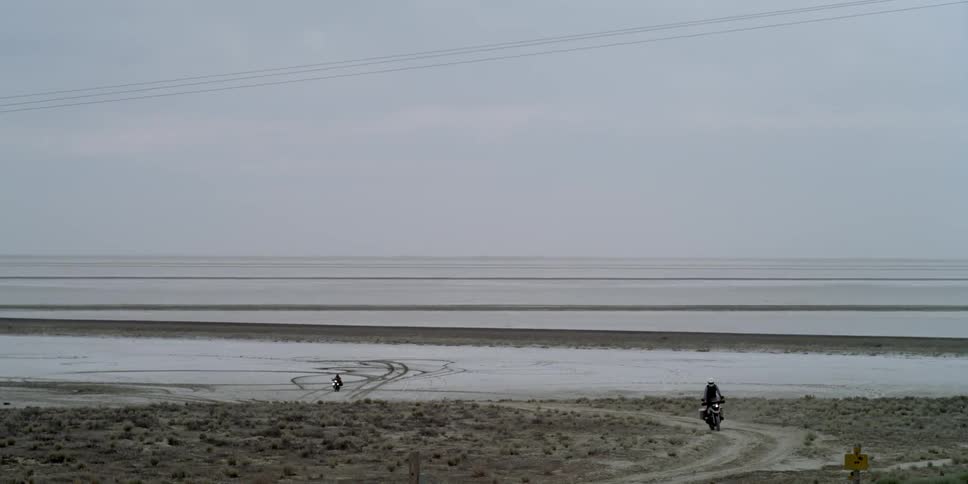 Two motorcycles riding on a salt flats and a dirt road