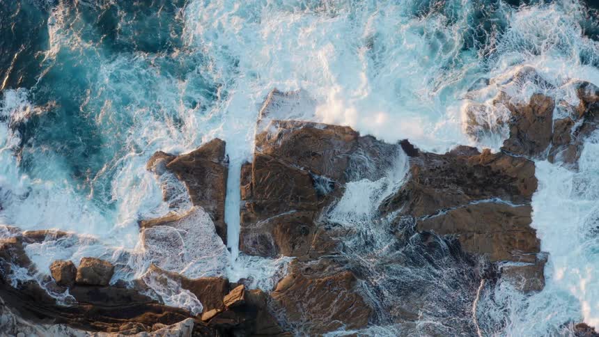 Strong ocean waves crash onto rocky terrain