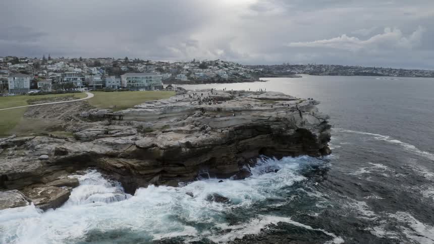 Aerial view of people standing on the cliff while foamy ocean waves crash against the rocks