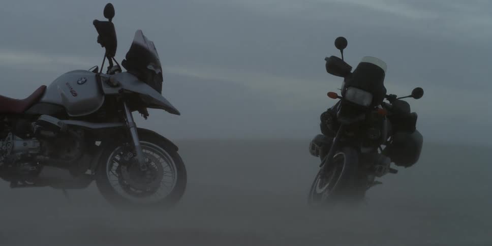 Windswept sand blows at the wheels of two parked motorcycles