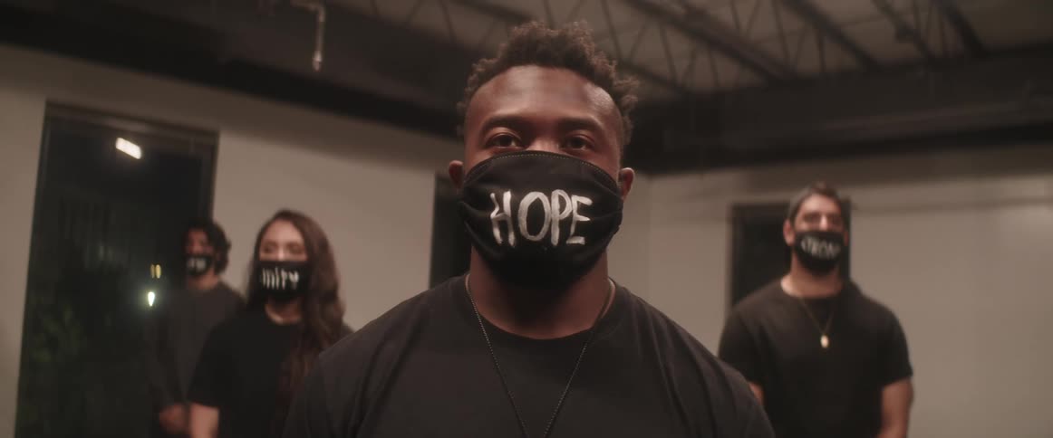 People wearing face masks with words on them stand in room