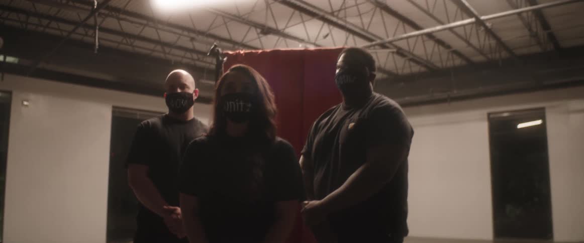 Group of three people wearing face masks and black shirts stand in front of red curtain in empty room