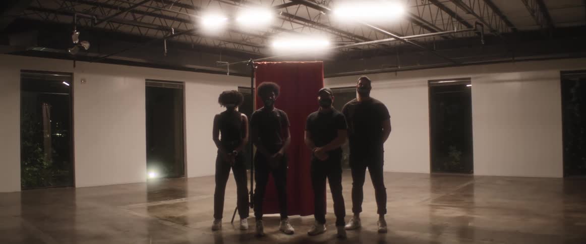 Four people stand in front of a red curtain in an empty room with glossy floors and multiple floor to ceiling windows