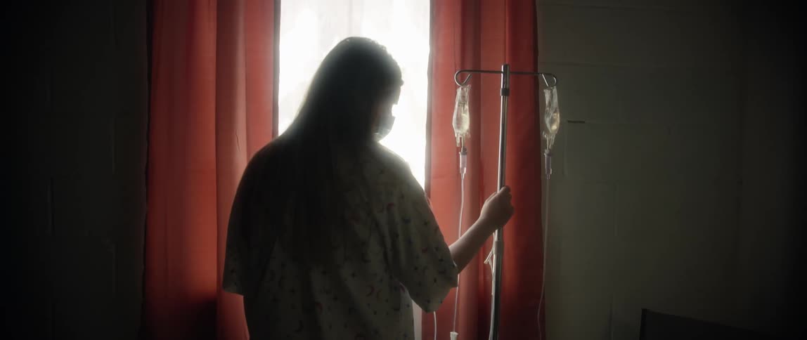 Patient standing in front of a window holding a stand with drip bags in a hospital room