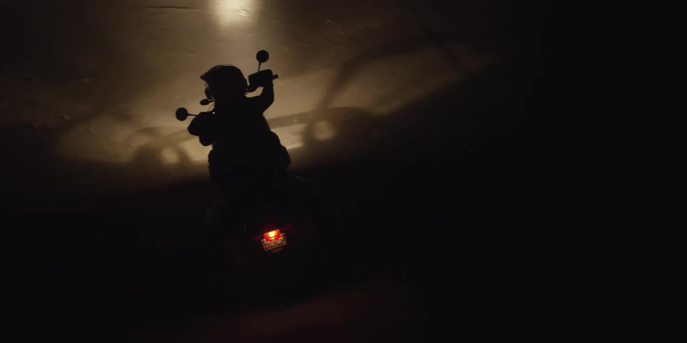 A motorcycle turns onto a dirt road at night