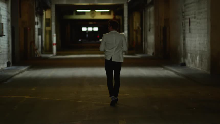 A man walks downs a street smoking and carrying a bottle of wine and then turns a corner and runs