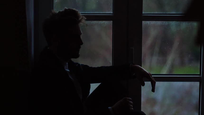 Man sitting on windowsill is silhouetted against outside
