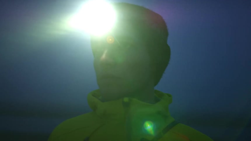 A man with a hat and a flashlight on his head looking around with the sky in the background