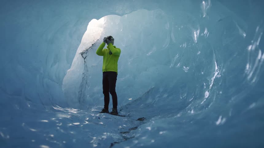 A photographer standing in a tunnel of ice raises his camera to take a photograph