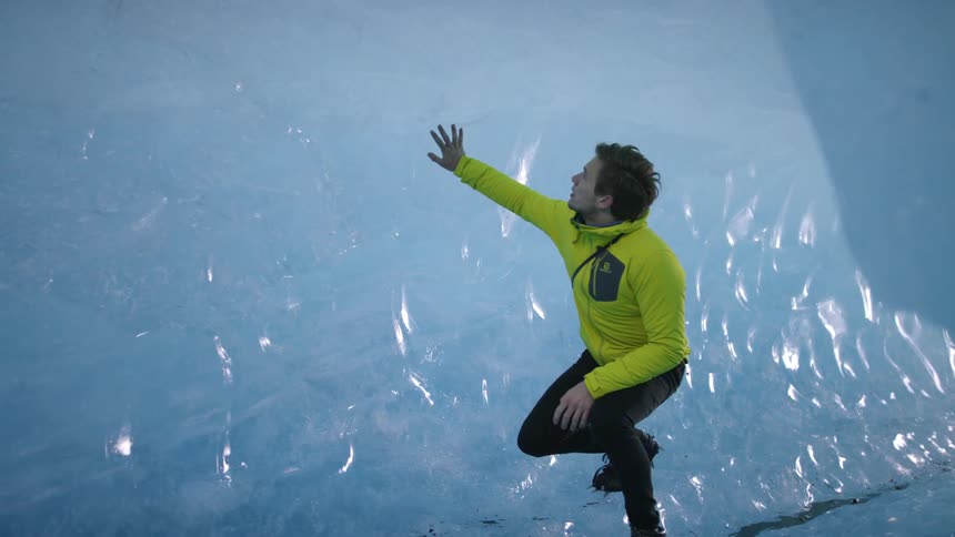 Man with a camera on a strap hanging over his shoulder walks through an ice tunnel