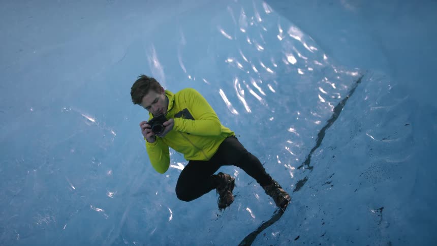 Man wearing cleats crouches in ice cave taking pictures