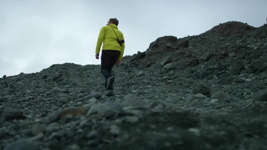 A man carrying a camera walks up a rocky hill