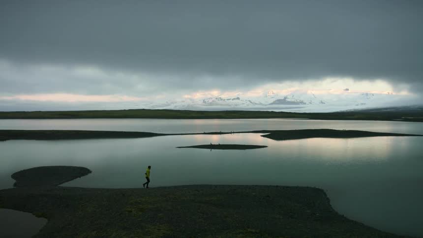 Person walks along lake shore under cloudy sky