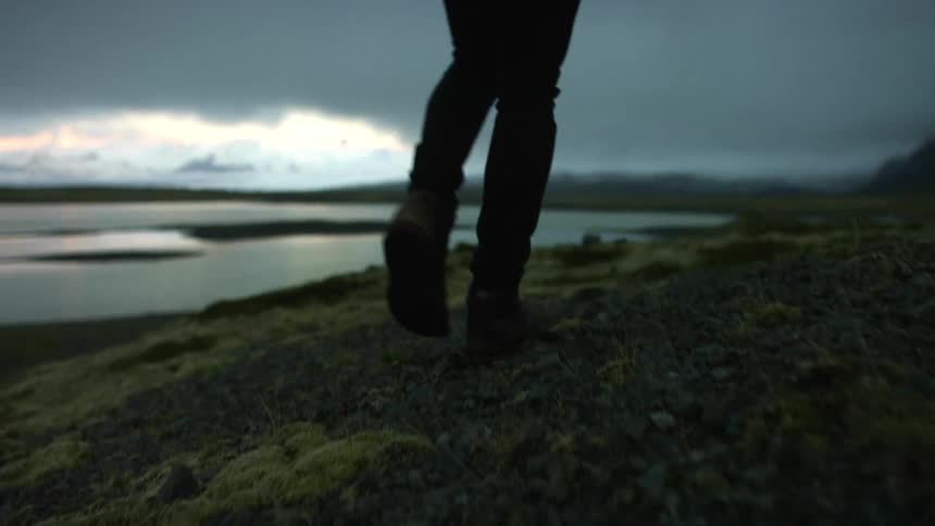 A man with a camera over his shoulder walks towards the shore