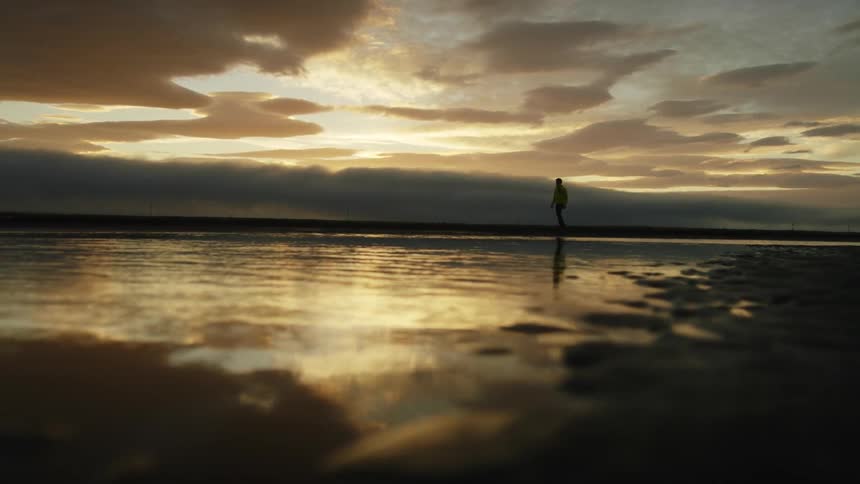 A silhouetted person walks next to a lake at sunset