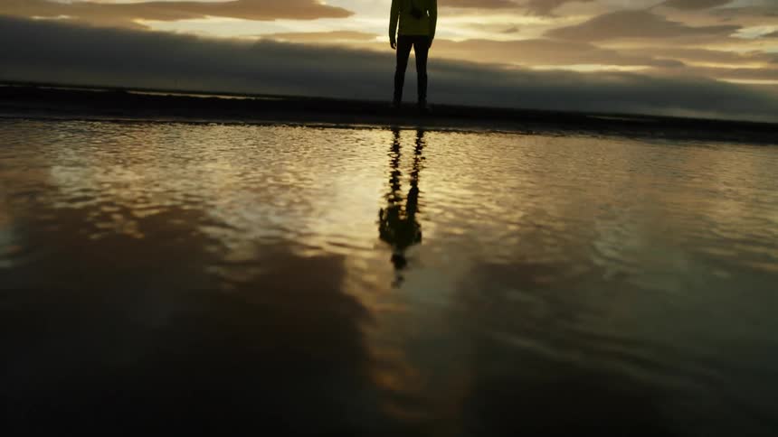 A man with a camera standing by a body of water with the sky and clouds in the background
