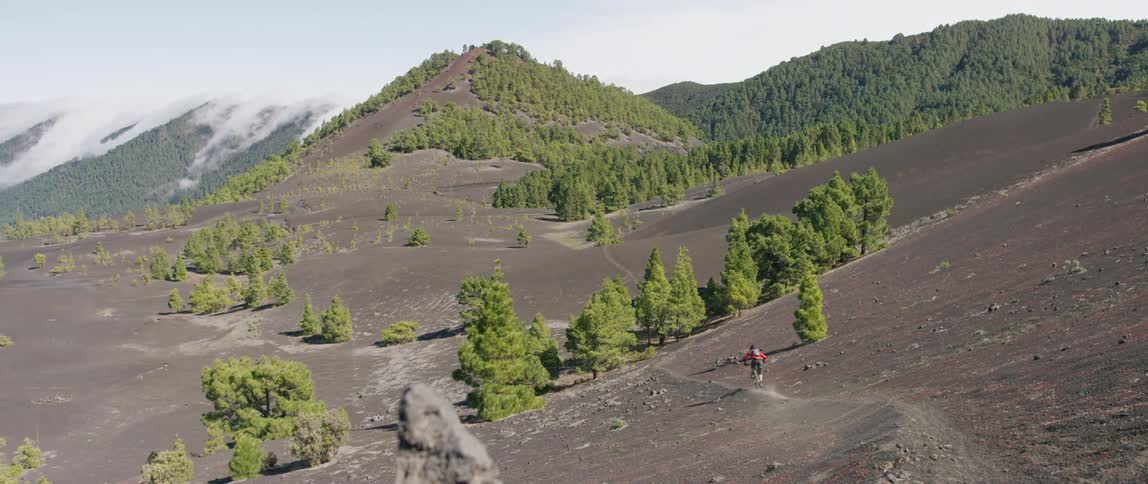 A mountain biker rides a bike along a dusty slope in the mountains during the day