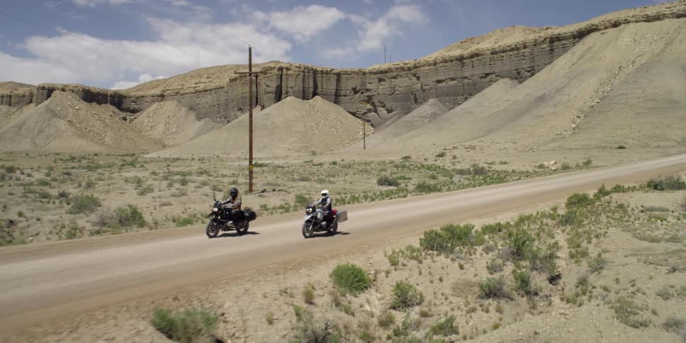 Two people ride bikes down a desert road